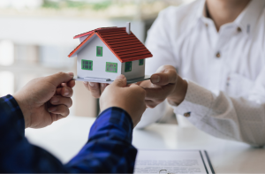 Symbolische Übergabe einer geerbten Immobilie zwischen zwei Personen mit einem Modellhaus.
